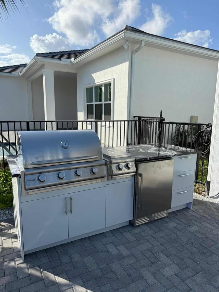 Outdoor kitchen with white waterproof cabinets, quartz countertop, and Blazer stainless steel grill. Designed and built by Evolux Cabinets for durable outdoor living.