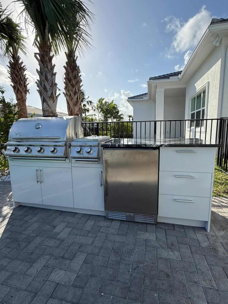 Outdoor kitchen with white waterproof cabinets, quartz countertop, and Blazer stainless steel grill. Designed and built by Evolux Cabinets for durable outdoor living.