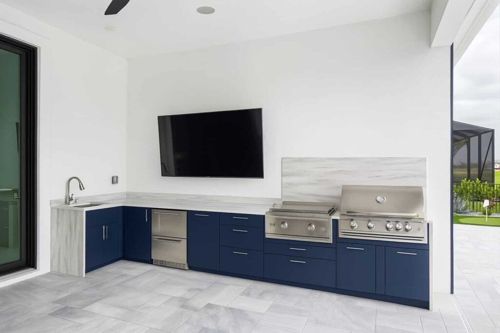 Outdoor kitchen with navy blue PVC and StarBoard waterproof cabinets, Durasing countertop and backsplash, and Blazer stainless steel grill. Designed and built by Evolux Cabinets for luxury outdoor spaces.