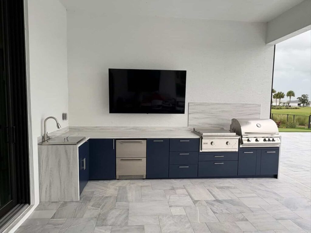 Outdoor kitchen with navy blue PVC and StarBoard waterproof cabinets, Durasing countertop and backsplash, and Blazer stainless steel grill. Designed and built by Evolux Cabinets for luxury outdoor spaces.