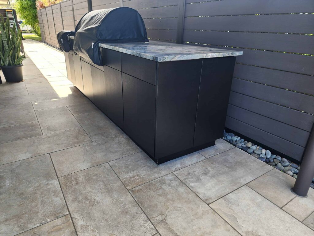 Outdoor kitchen with black PVC and StarBoard waterproof cabinets, quartz countertop, and Blazer stainless steel grill. Designed and built by Evolux Cabinets for luxury outdoor living.