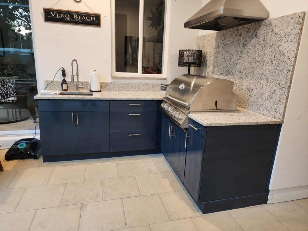 Outdoor kitchen with navy blue waterproof cabinets, quartz countertop and backsplash, and Blazer stainless steel grill. Designed and built by Evolux Cabinets for elegant and durable living spaces.
