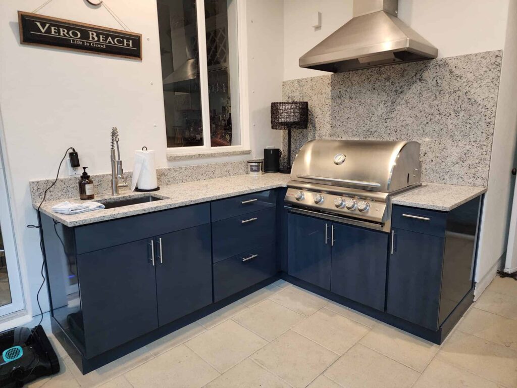 Outdoor kitchen with navy blue waterproof cabinets, quartz countertop and backsplash, and Blazer stainless steel grill. Designed and built by Evolux Cabinets for elegant and durable living spaces.