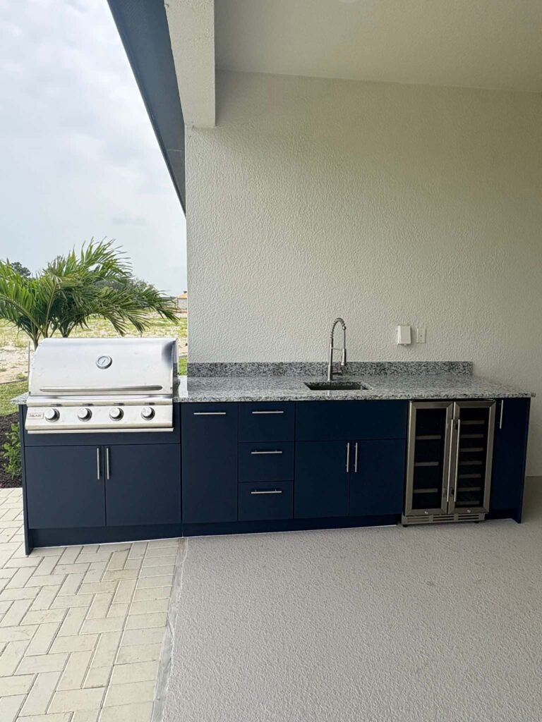 Outdoor kitchen with navy blue PVC and StarBoard waterproof cabinets, quartz countertop, and Blazer stainless steel grill. Designed and built by Evolux Cabinets for elegant and durable outdoor living.
