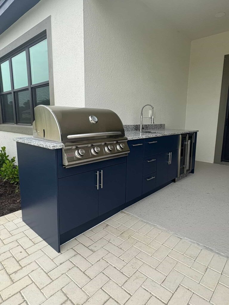 Outdoor kitchen with navy blue PVC and StarBoard waterproof cabinets, quartz countertop, and Blazer stainless steel grill. Designed and built by Evolux Cabinets for elegant and durable outdoor living.