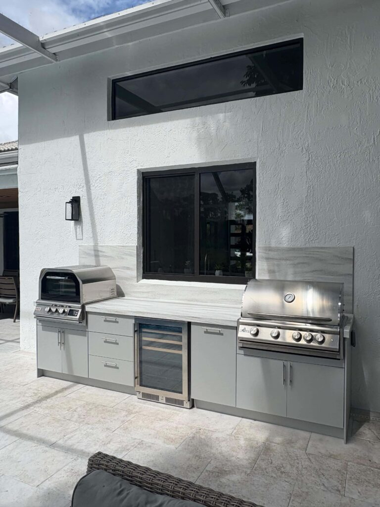 Modern outdoor kitchen with light gray waterproof cabinets, Durasing countertop, marble backsplash, and stainless steel grill. Built by Evolux Cabinets for durable outdoor living.