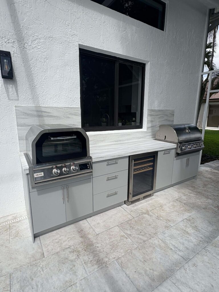 Modern outdoor kitchen with light gray waterproof cabinets, Durasing countertop, marble backsplash, and stainless steel grill. Built by Evolux Cabinets for durable outdoor living.